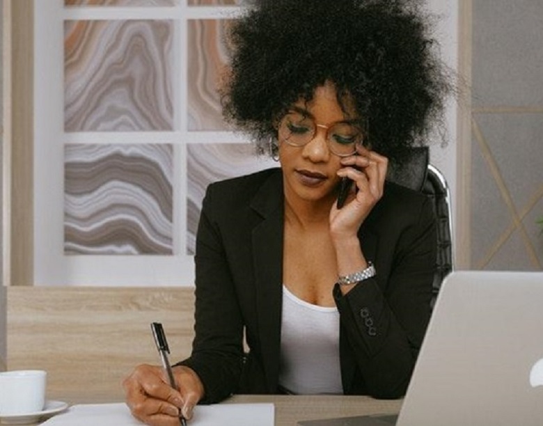 Beautiful black female who is an MBA grad on the phone taking notes