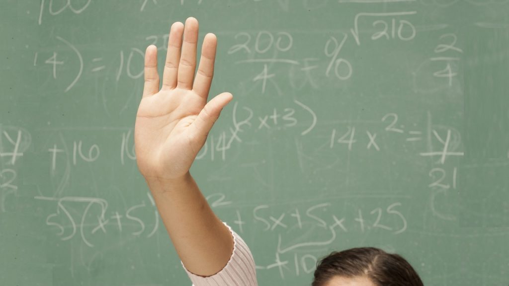 A student's hand raised in front of a chalk board