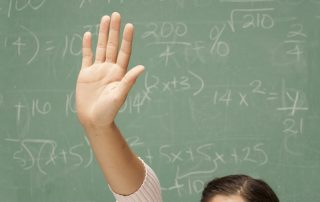 A student's hand raised in front of a chalk board